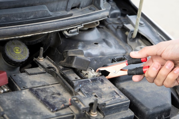 Un mécanicien automobile utilise des câbles de démarrage de batterie pour charger une batterie déchargée