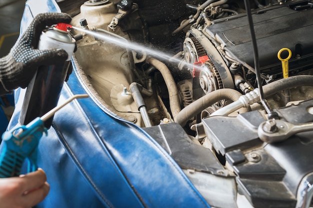 Un mécanicien automobile utilise un spray pour nettoyer les composants du véhicule avant de remplacer la courroie de distribution