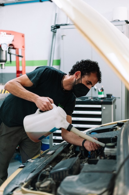 mécanicien automobile vérifiant le niveau d'huile portant un masque chirurgical