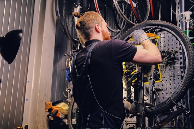 Mécanicien barbu réparant un pneu de roue de bicyclette dans un atelier. Vue arrière, manuel d'entretien.