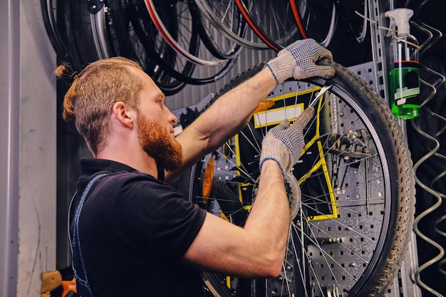 Mécanicien barbu réparant un pneu de roue de bicyclette dans un atelier. Vue arrière, manuel d'entretien.