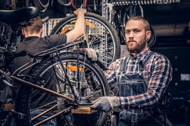 Mécanicien barbu à tête rouge fixant le dérailleur arrière d'un vélo dans un atelier.