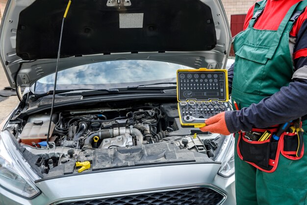 Mécanicien avec boîte à outils posant près de la voiture avec capot ouvert