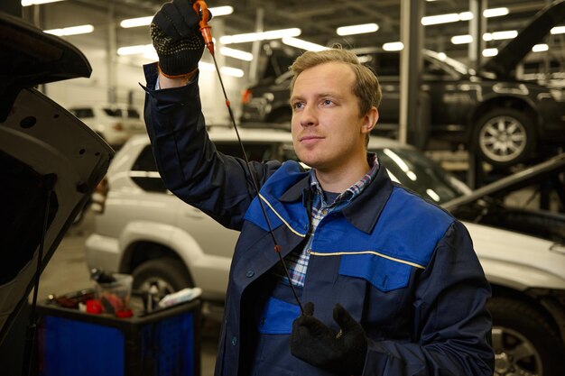 Mécanicien dans un garage examinant la jauge d'huile moteur de voiture vérifiant le niveau d'huile moteur dans une voiture. Technicien ingénieur automobile dans l'atelier de réparation automobile. Concept d'entretien automobile et de service automobile