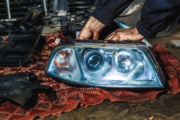 Un mécanicien dans son atelier répare un phare de voiture. Concept de service de voiture.