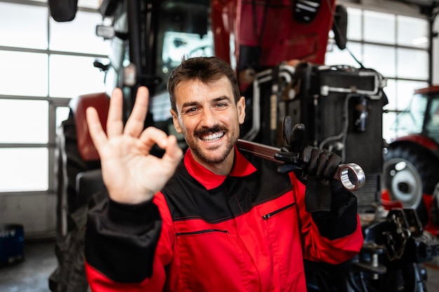 Photo mécanicien debout devant le tracteur et montrant un signe de geste d'accord