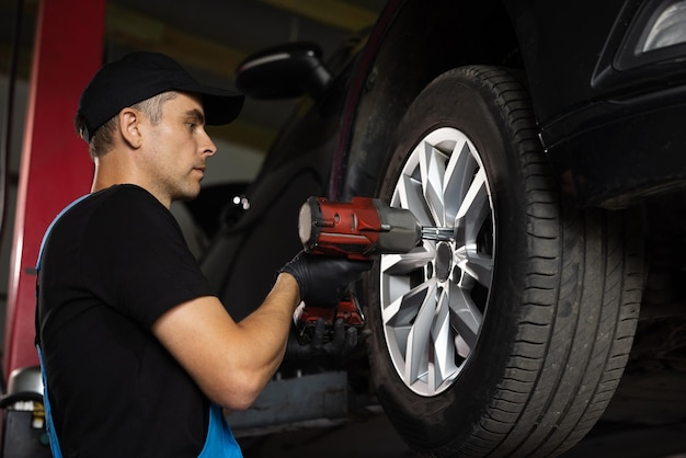 Le mécanicien dévisse les écrous de roue avec une clé à chocs pneumatique. Le réparateur travaille dans un service de voiture moderne