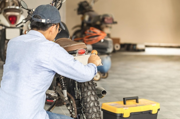 Mécanicien fixant une moto dans un garage d'atelier Homme réparant une moto dans un atelier de réparation Concepts de réparation et d'entretien