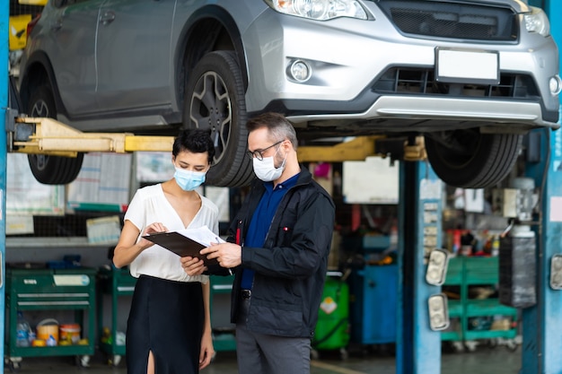 Mécanicien homme et femme client portant un masque médical de protection contre le coronavirus et vérifier l'état de la voiture avant la livraison.
