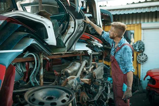 Mécanicien masculin choisissant la porte sur la casse de voiture. Déchets d'automobiles, ordures de véhicules, ordures d'automobiles. Transport abandonné, endommagé et écrasé, casse