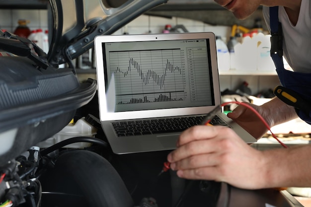 Photo mécanicien avec ordinateur portable faisant des diagnostics de voiture à l'atelier de réparation automobile agrandi
