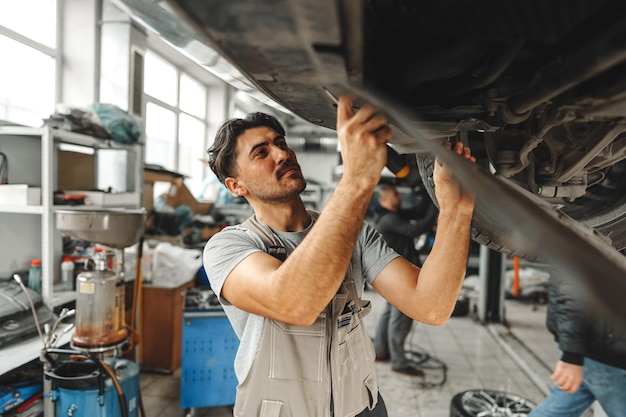 Mécanicien ouvrier travaillant sous la voiture dans un atelier de réparation automobile