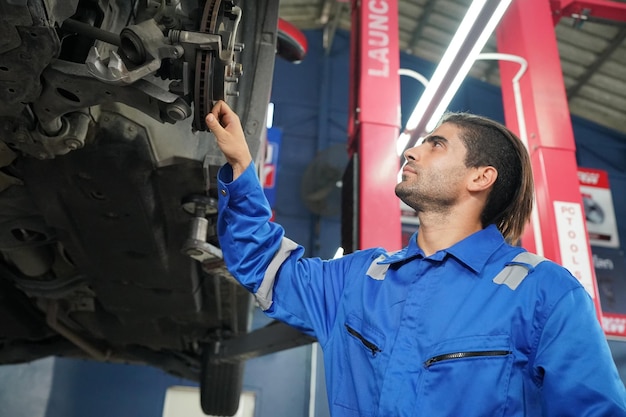 Mécanicien en salopette bleue vérifiant le bon fonctionnement du moteur de la voiture