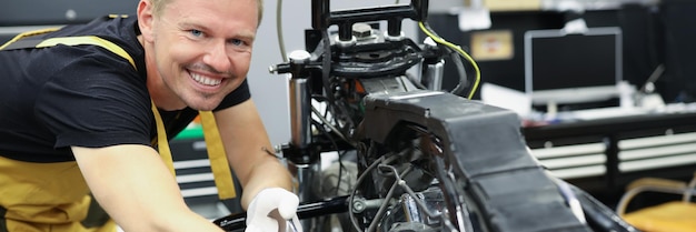 Le mécanicien de serrurier avec la clé se tient à côté du concept de réparation de moto de moteur de moto