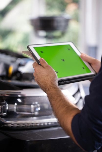 Le mécanicien de service de voiture utilise un ordinateur tablette avec une maquette d'écran vert chroma key qui est pointée