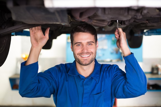 Mécanicien souriant à la caméra sous la voiture