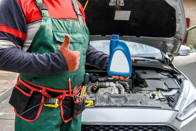 Mécanicien tenant des bouteilles avec de l'huile près du moteur de la voiture