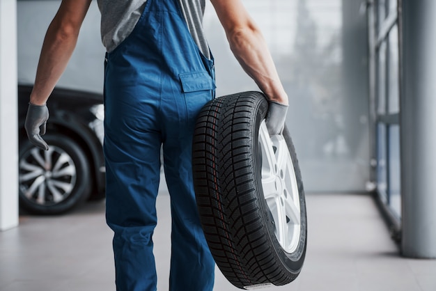 Mécanicien tenant un pneu de pneu au garage de réparation. remplacement des pneus hiver et été