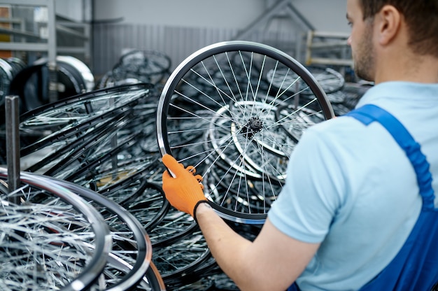 Mécanicien en uniforme tient la roue de bicyclette sur l'usine. Assemblage de jantes et rayons de vélo en atelier, installation de pièces de vélo