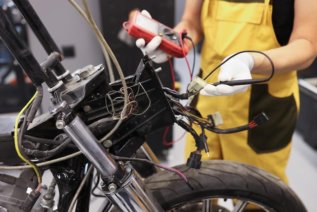 Un mécanicien utilisant un multimètre vérifie le niveau de tension sur la batterie de la moto dans le garage de motos