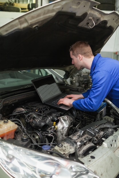 Mécanicien utilisant un ordinateur portable sur le moteur de la voiture