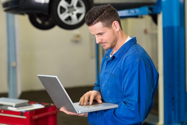 Mécanicien utilisant un ordinateur portable pour travailler au garage de réparation