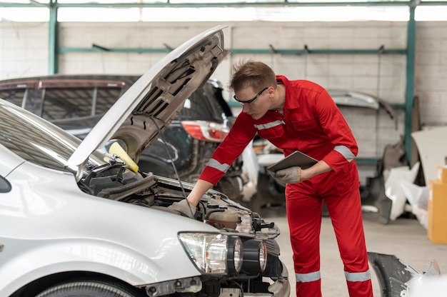 Mécanicien utilisant la tablette de vérification et d'entretien du moteur de voiture de réparation au service de garage automobile