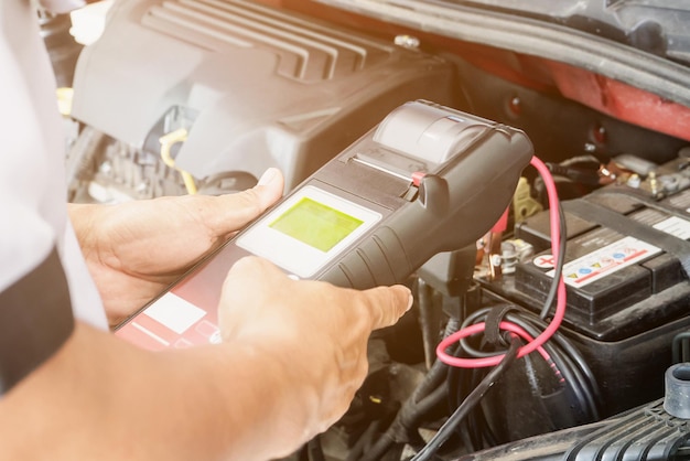 Un mécanicien utilise un voltmètre vérifiant la tension de la batterie de la voiture dans un centre de service automobile