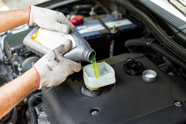 Un mécanicien de voiture verse de l'huile d'une bouteille dans le moteur à travers un entonnoir