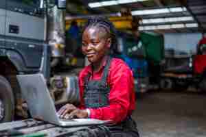 Photo une mécanicienne afro-américaine souriante améliore le processus de réparation avec un ordinateur portable assi