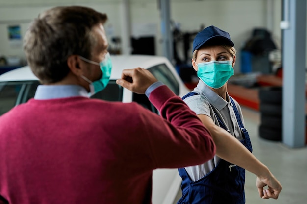 Une mécanicienne automobile et son client saluent avec les coudes tout en portant des masques de protection dans un atelier de réparation automobile pendant l'épidémie de coronavirus