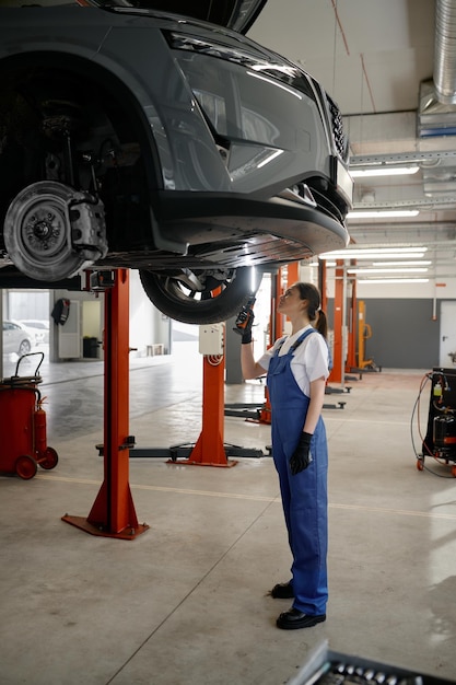 Une mécanicienne examine une voiture suspendue à un ascenseur à l'aide d'une lampe de poche