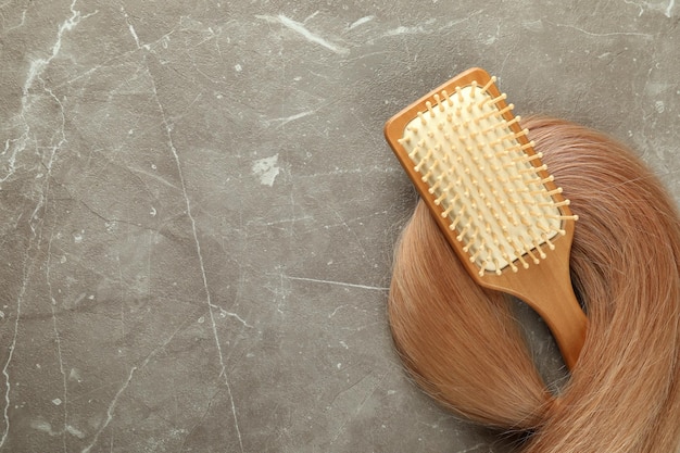 Une mèche de cheveux féminins avec brosse à cheveux sur fond texturé gris
