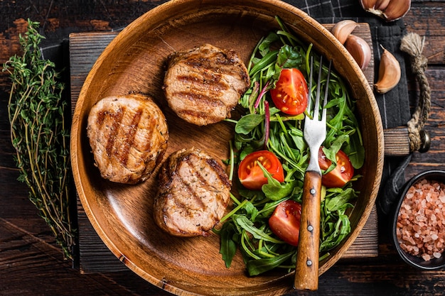 Médaillons de porc rôti steaks de filet de filet avec salade de légumes dans une assiette en bois Fond en bois Vue de dessus