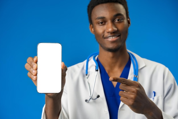 Médecin africain joyeux utilisant un téléphone portable sur fond de studio bleu