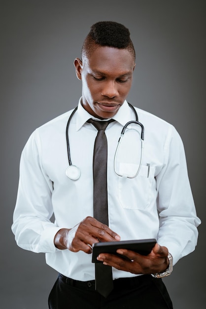 Médecin africain avec stéthoscope debout et utilisant une tablette numérique.