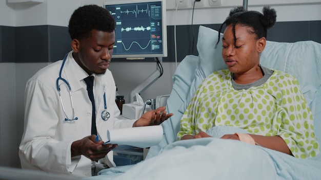 Médecin afro-américain consultant un patient avec un sac d'égouttement IV. Médecin généraliste vérifiant les dossiers d'examen pour traiter une personne malade, pour guérir avec un traitement sur ordonnance et des médicaments