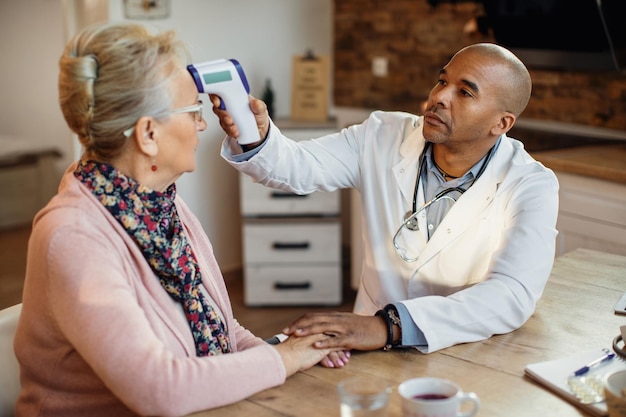 Médecin afro-américain mesurant la température d'une femme âgée lors d'une visite à domicile