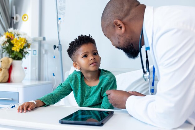 Photo un médecin afro-américain souriant et un garçon patient discutent à l'hôpital.