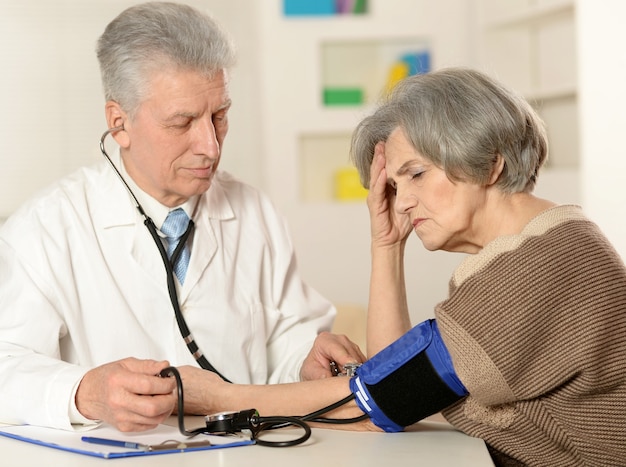 Médecin âgé mesurant la tension artérielle à la femme âgée