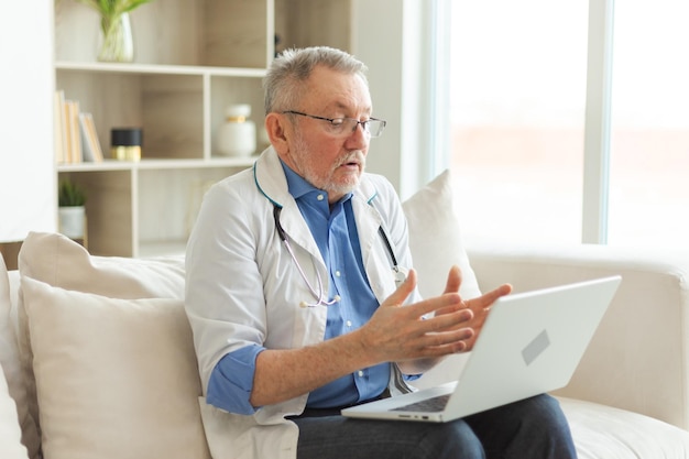 Un médecin âgé avec un ordinateur portable parle par appel vidéo a une consultation avec un patient professionnel âgé