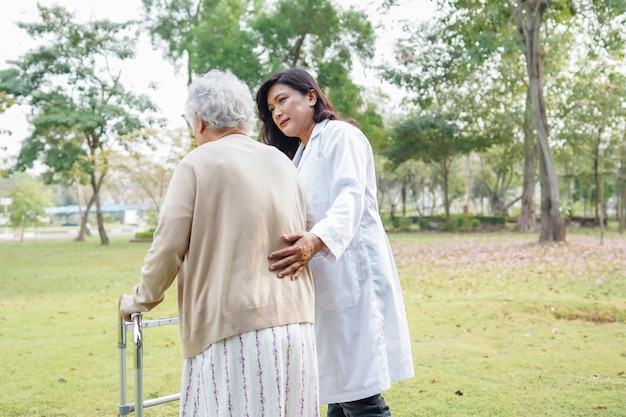 Médecin aidant une femme senior asiatique à l'aide de la marchette en marchant au parc.