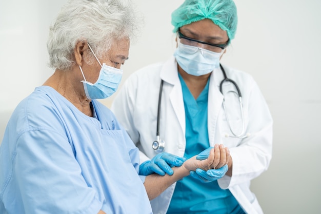 Un médecin aide une patiente asiatique âgée portant un masque facial à l'hôpital pour protéger le coronavirus