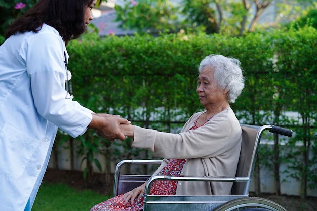 Un médecin aide une patiente handicapée asiatique âgée assise sur un fauteuil roulant dans le concept médical du parc