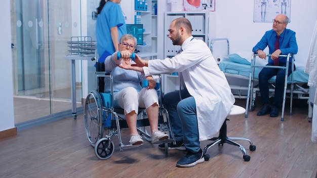 Un médecin aide une vieille femme handicapée en fauteuil roulant à regagner de la force musculaire dans une clinique privée de récupération. Personne invalide utilisant des haltères pour faire de l'exercice. Hôpital de réadaptation, travaillant avec seni paralysé