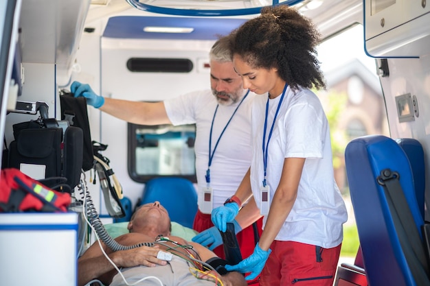 Photo médecin ambulancier enveloppant le brassard de tensiomètre autour du bras supérieur de l'homme malade supervisé par son collègue