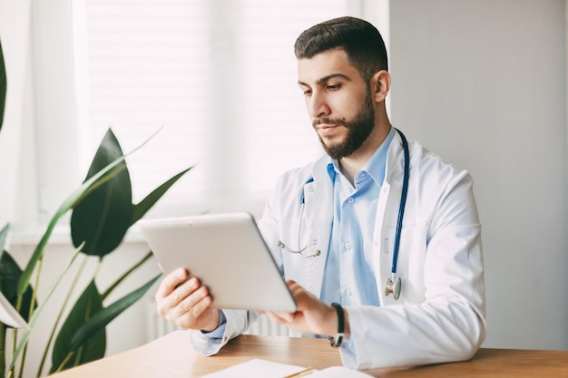 Un médecin d'apparence orientale travaille concentré sur une tablette assis à une table