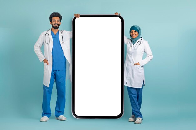 Photo médecin arabe femme et homme en uniforme debout près d'un grand smartphone vierge