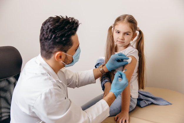 Un médecin arabe ou turc donne à une petite fille un vaccin contre le coronavirus. Fille souriante. Photo de haute qualité