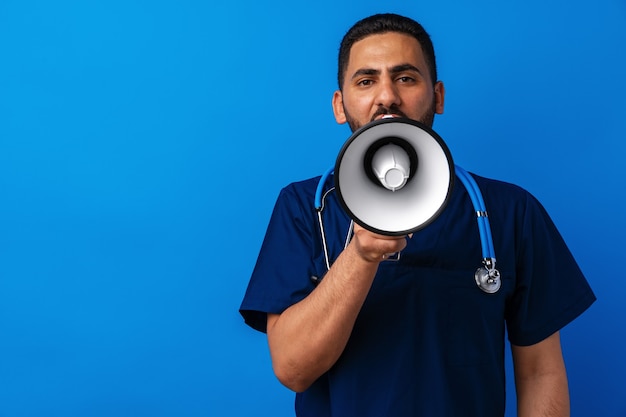 Médecin arabe en uniforme criant dans un mégaphone sur fond bleu